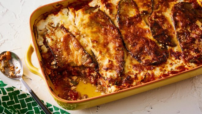 Moussaka served in a yellow baking dish with a portion removed to see the filling