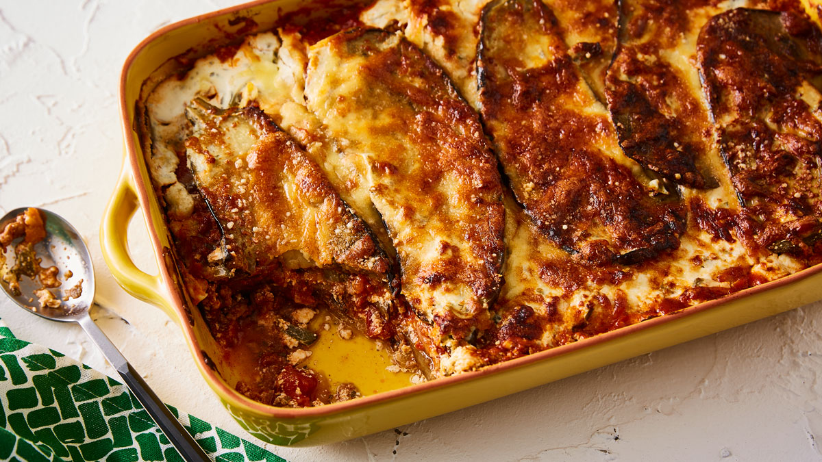 Moussaka served in a yellow baking dish with a portion removed to see the filling