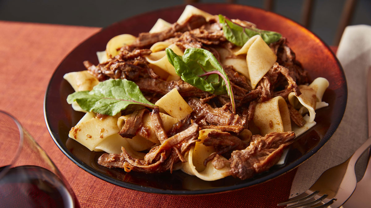 Mulled Spiced Beef Ragu served in a red bowl and topped with leafy greens