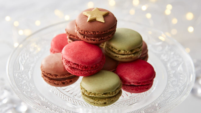 Festive Macaron Trio, served on a glass cake dish, piled on top of one another and topped with a gold star