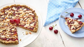 No Bake Cherry Bakewell served on a white dish, with a sliced removed and to the side on a blue plate