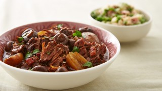 Classic Beef Stew served in a white bowl topped with parsley, with a bowl of colcannon mash in the background