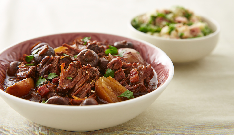 Classic Beef Stew served in a white bowl topped with parsley, with a bowl of colcannon mash in the background