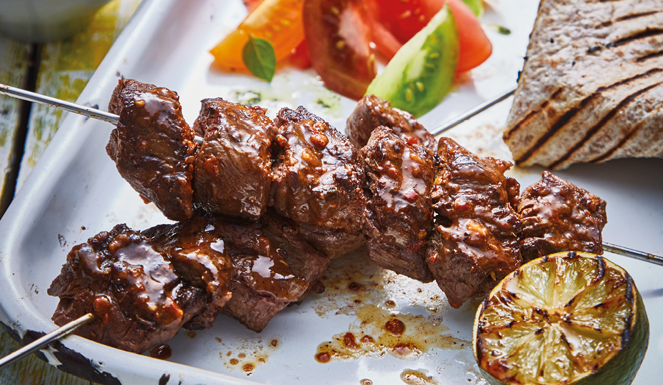 Brazilian Churrasco Beef Kebabs served on a white plate with coloured tomato salad