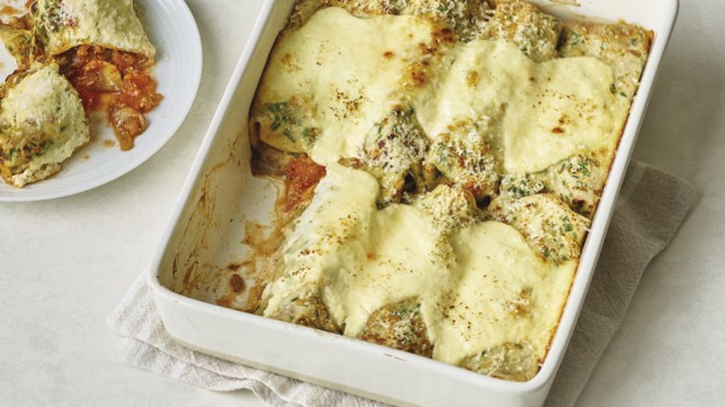 Beef Ragu Pancake Cannelloni served in a casserole dish, with a portion placed on a plate to the left, cut open to see the filling