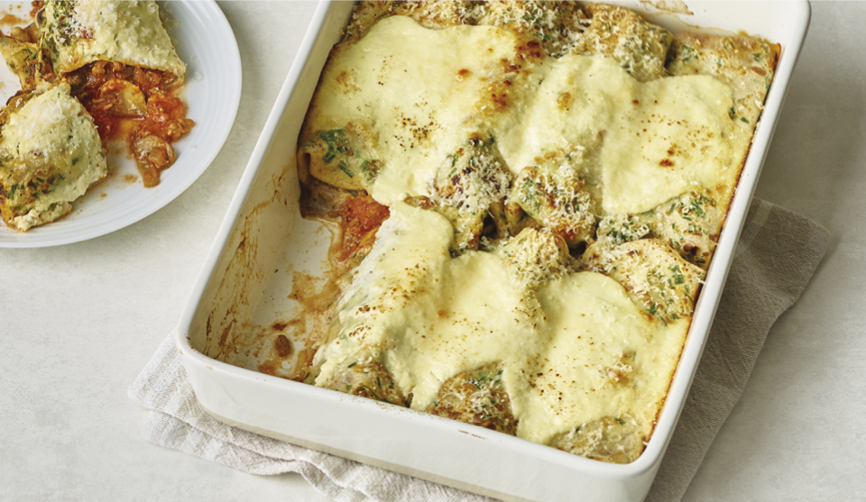Beef Ragu Pancake Cannelloni served in a casserole dish, with a portion placed on a plate to the left, cut open to see the filling