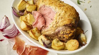 Roast Lamb with a Parmesan Crust, served on a white dish with roast potatoes. The lamb has been sliced