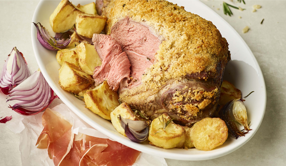 Roast Lamb with a Parmesan Crust, served on a white dish with roast potatoes. The lamb has been sliced