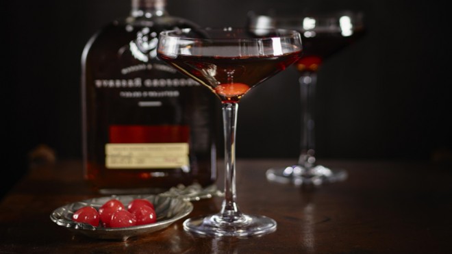 The Perfect Manhattan served in two glasses next to a dish of maraschino cherries