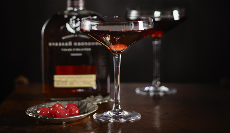 The Perfect Manhattan served in two glasses next to a dish of maraschino cherries