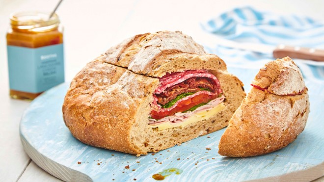 Picnic Loaf, sliced to see the filling, served on a blue board