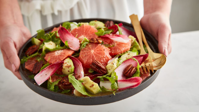 Pink Grapefruit, Candied Pecan and Avocado Sald served in a grey bowl with a gold fork and spoon