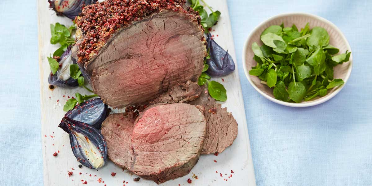 Roast Topside of Beef with Pink Peppercorn Crust served sliced on a white board