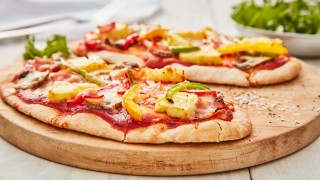 Pitta Pizza topped with vegetables served on a wooden board with a slice removed