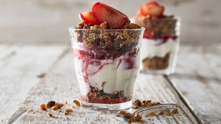 Poached Plums with Quinoa Granola served in glasses with granola scattered around the glasses