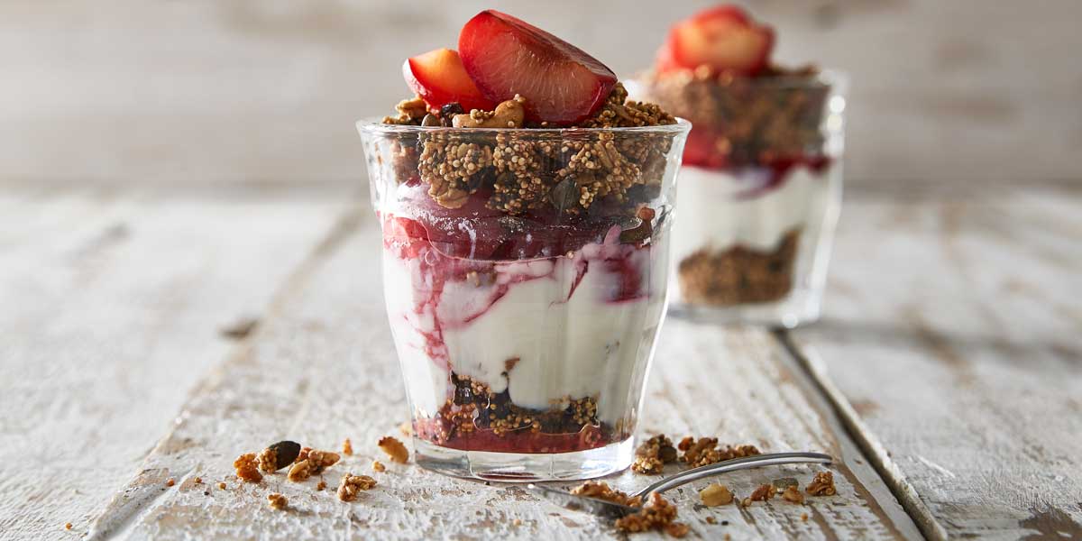 Poached Plums with Quinoa Granola served in glasses with granola scattered around the glasses