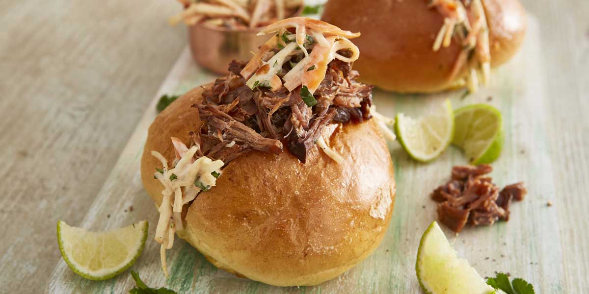 Pulled Beef and 'Slaw Butty, served on a wooden board, with wedges of lime