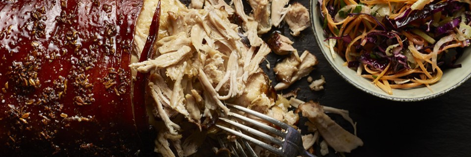 Pulled Pork which has been shredded by two forks next to a bowl of crunchy coleslaw