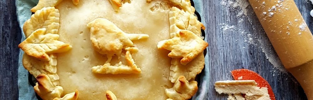 Apple and Pumpkin Spice Cheese Pie served on a blue tablecloth with a pastry bird and leaves on top