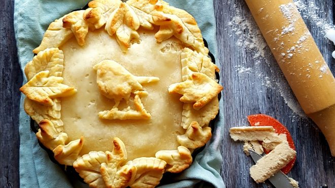 Apple and Pumpkin Spice Cheese Pie served on a blue tablecloth with a pastry bird and leaves on top