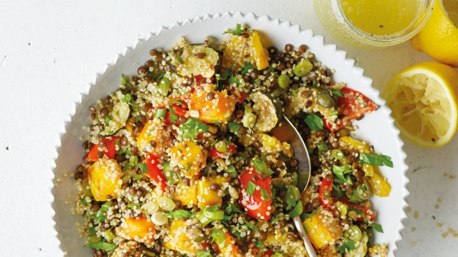 Quinoa, Roasted Vegetable and Puy Lentil Salad served in a white bowl, with sprinkled parsley and squeezed lemon wedges to the side