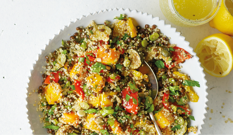 Quinoa, Roasted Vegetable and Puy Lentil Salad served in a white bowl, with sprinkled parsley and squeezed lemon wedges to the side