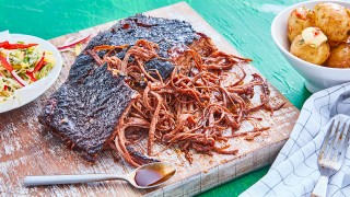 Sweet and Spicy BBQ Brisket served on a wooden board, with bowls of potatoes and salad