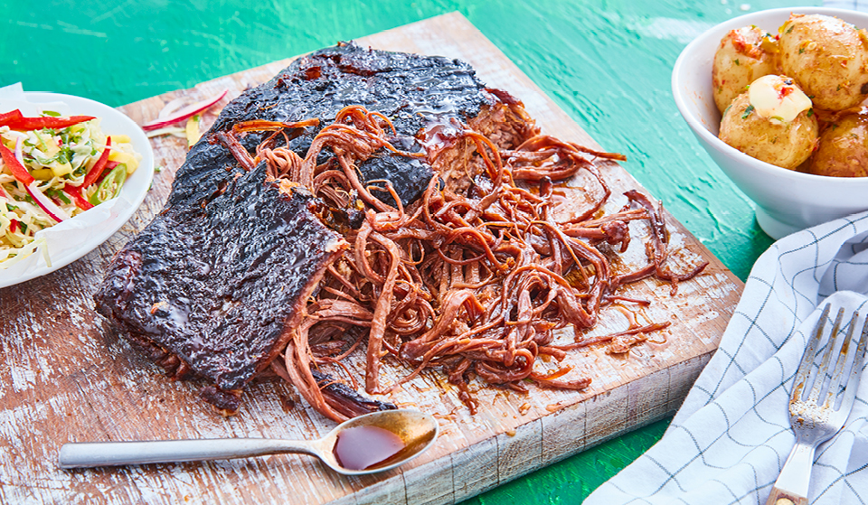 Sweet and Spicy BBQ Brisket served on a wooden board, with bowls of potatoes and salad