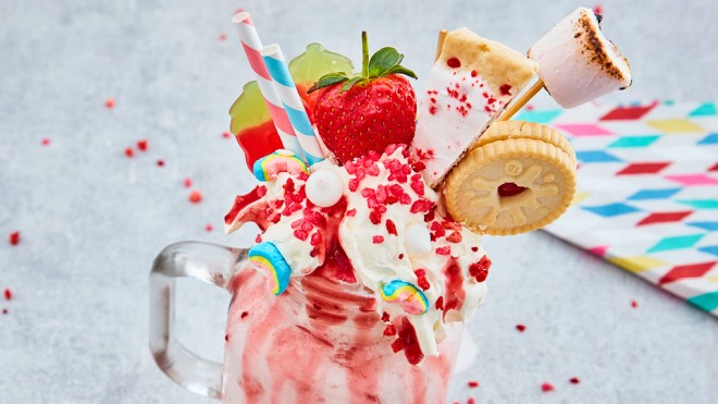 Boozy Milkshake served in a glass jar with whipped cream, sweets, strawberries and biscuits in the top