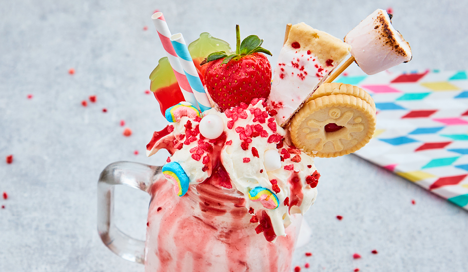 Boozy Milkshake served in a glass jar with whipped cream, sweets, strawberries and biscuits in the top