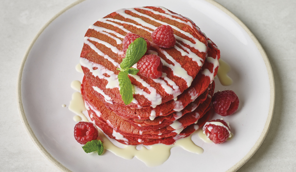 Red Velvet Pancakes with White Chocolate Sauce served on a white plate and topped with raspberries