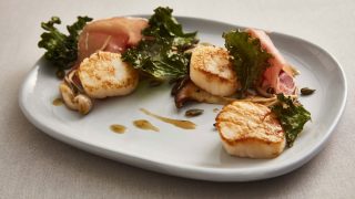 Scallops, Air-Dried Ham and Wild Mushrooms serve on a white plate with kale and olive oil