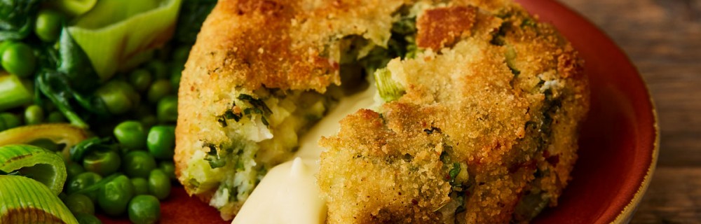 Smoked Haddock and Cheddar Cheese Fishcake served on a red plate with vegetables, the fishcake has been cut into for the cheese to pour out