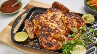 Spatchcock Chicken served on a baking tray with watercress and wedges of lime