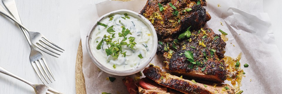 Spiced Butterflied Leg of Lamb sliced and served on a wooden board with greek yoghurt mixed with mint and parsley