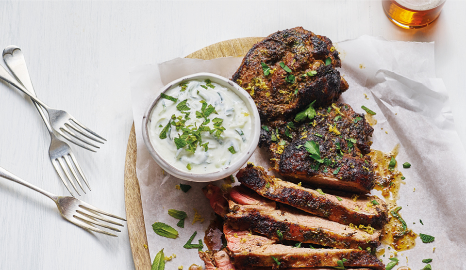 Spiced Butterflied Leg of Lamb sliced and served on a wooden board with greek yoghurt mixed with mint and parsley