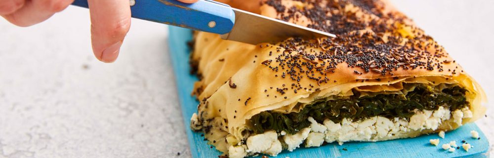 Spinach and Feta Filo Roll served on a small wooden board with a slice removed to see the filling