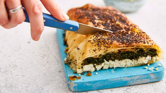 Spinach and Feta Filo Roll served on a small wooden board with a slice removed to see the filling