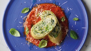 Spinach and Rocitta Pasta Roll sliced and oin top of the tomato sauce on a blue plate
