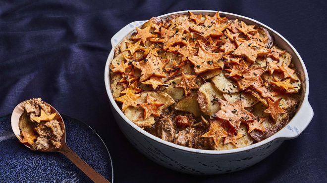 Star of the North Lamb Hotpot served in a casserole dish with a small amount of topping removed on a spoon to see the filling
