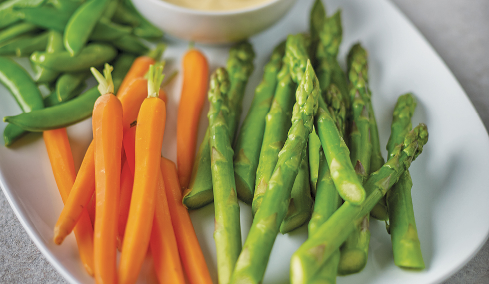 Simple Steamed Asparagus served on a white plate next to steamed carrots