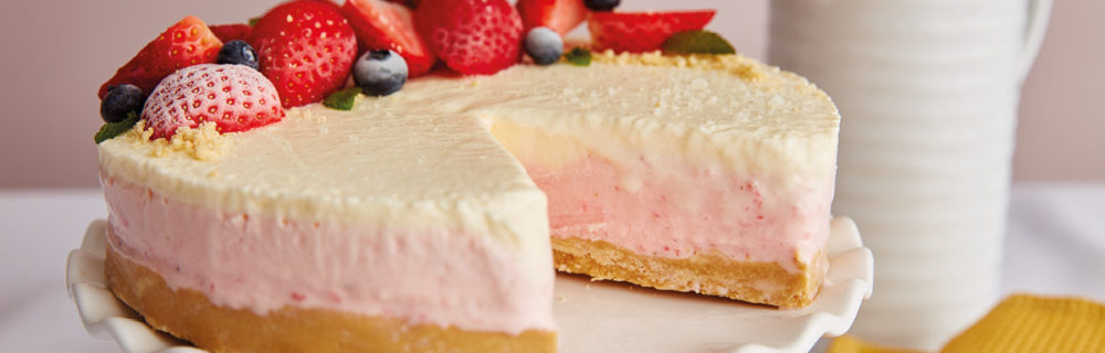 Strawberries and Cream Cheesecake served on a white cake dish with a slice removed to see the filling