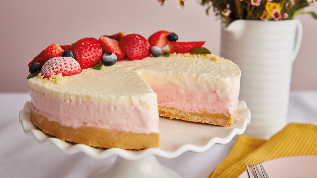 Strawberries and Cream Cheesecake served on a white cake dish with a slice removed to see the filling