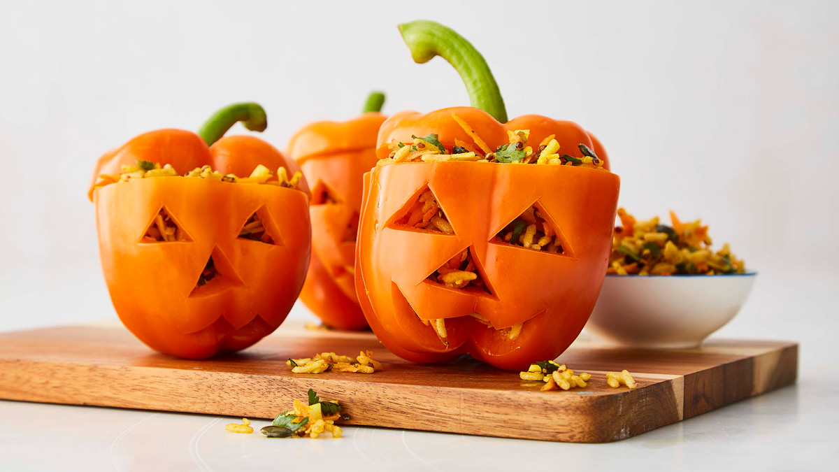 Stuffed Pumpkin Peppers served on a wooden board with faces cut out on the peppers