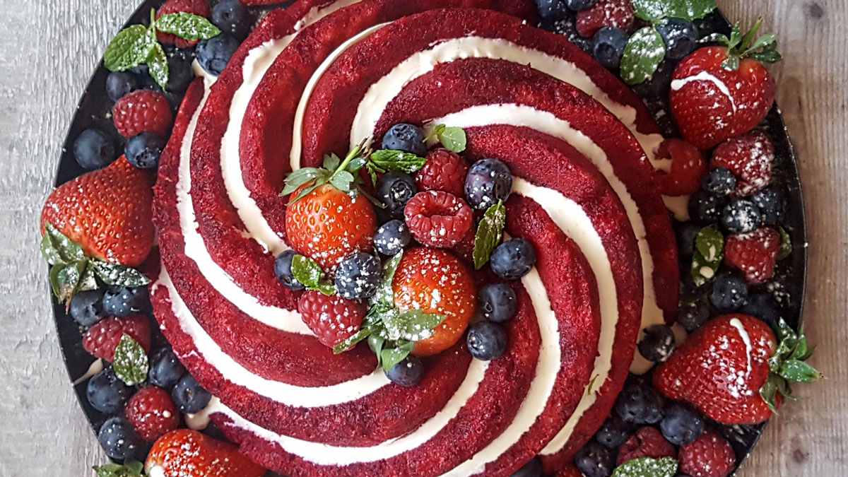 Summer Pudding served on a black plate, drizzled with cream and surrounded by fresh berries