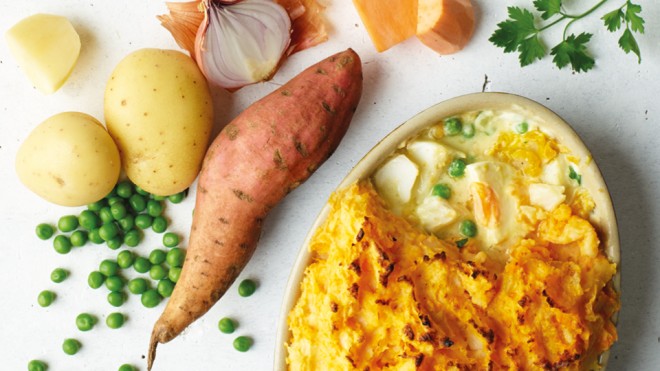 Smoked Fish Pie with Sweet Potato Topping with a portion missing to see the filling, placed next to various vegetables used in the recipe