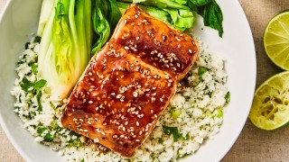 Teriyaki Salmon Cauliflower Rice served alongside pak choi in a white bowl with lime wedges on the side