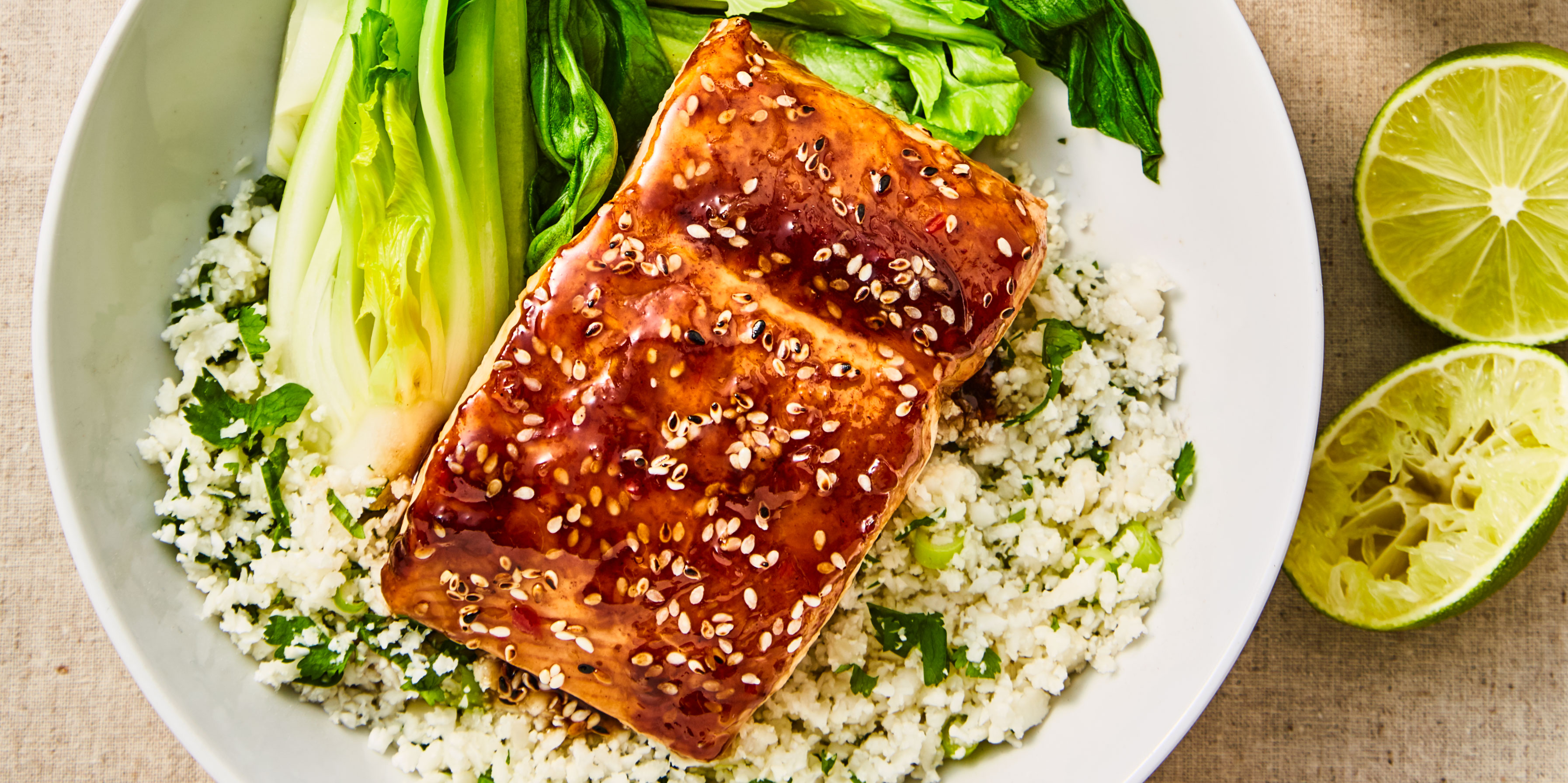 Teriyaki Salmon Cauliflower Rice served alongside pak choi in a white bowl with lime wedges on the side