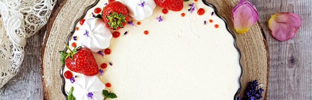 Cream Tea Cheesecake served on a wooden board, topped with strawberries and mini meringues