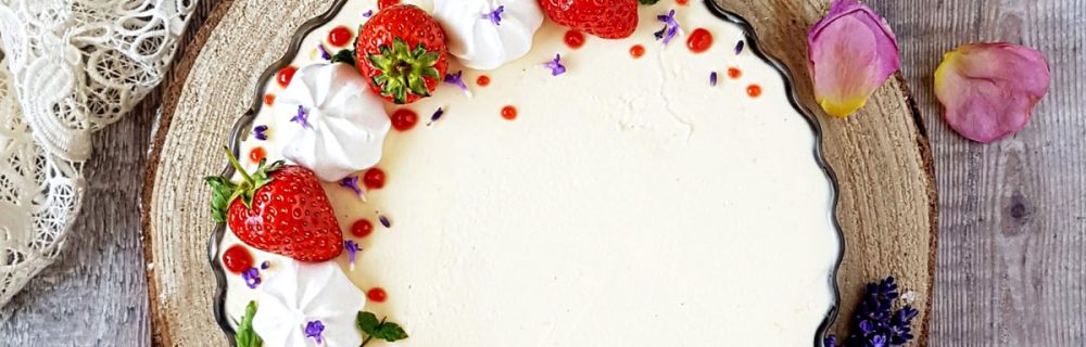 Cream Tea Cheesecake served on a wooden board, topped with strawberries and mini meringues